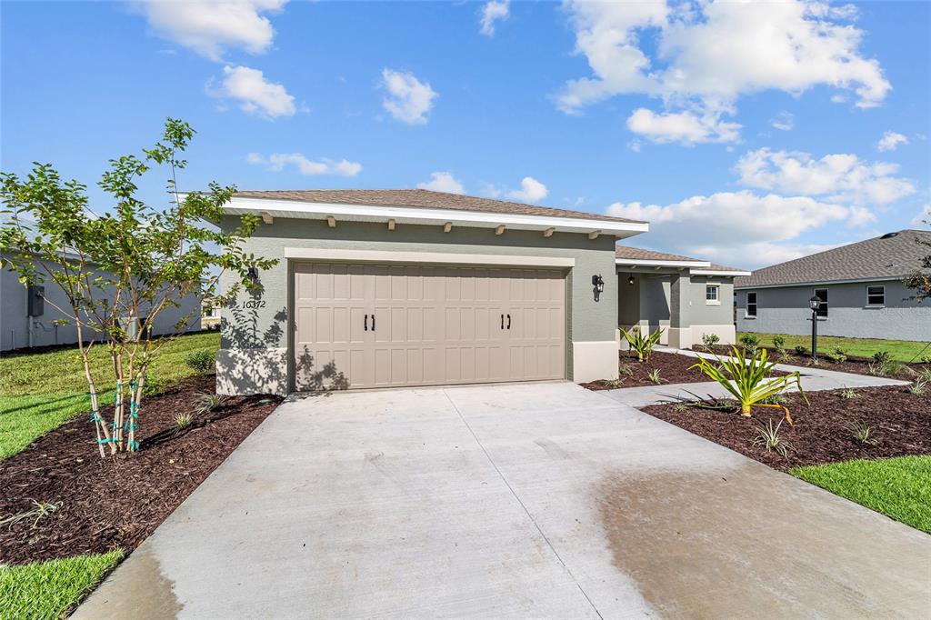 A single-story house features a tan garage door, a concrete driveway, and landscaped mulch beds — 10372 SW 105TH COURT, OCALA, FL