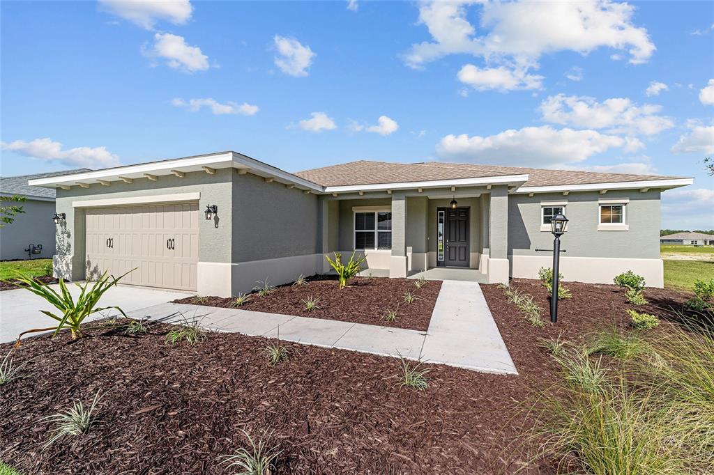 A single-story house with a tan garage, gray stucco exterior, and a concrete walkway — 10372 SW 105TH COURT, OCALA, FL