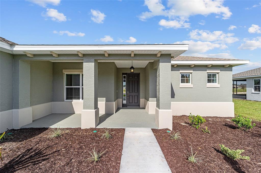 A front view of a house exterior featuring a covered porch and a dark door — 10372 SW 105TH COURT, OCALA, FL
