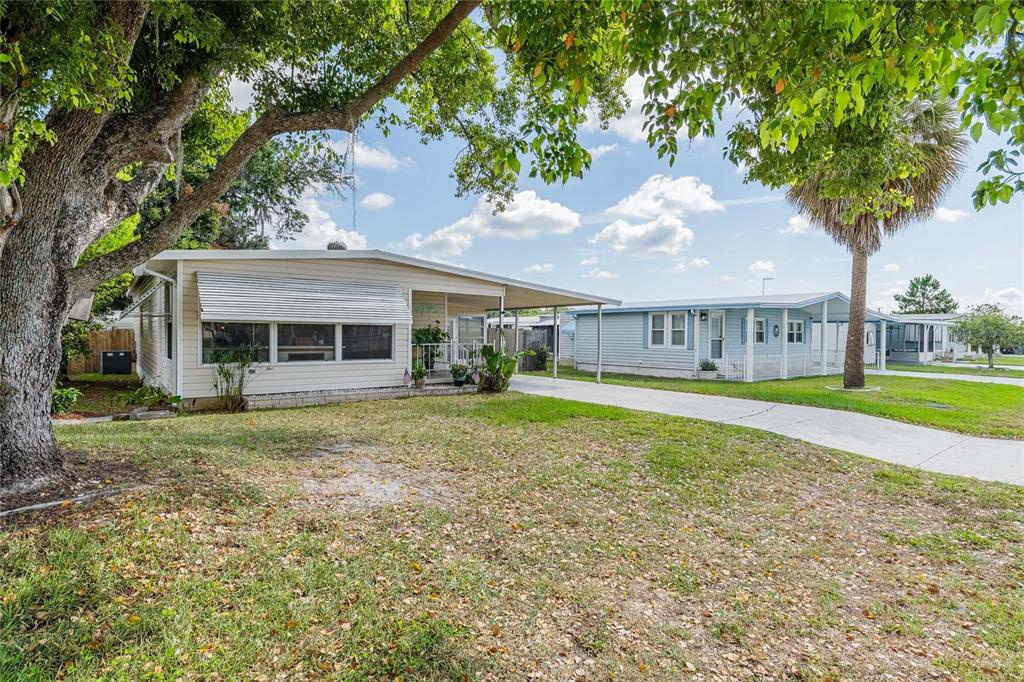 A light-colored mobile home with a carport and a large tree in the front yard — 36749 JODI AVENUE, ZEPHYRHILLS, FL