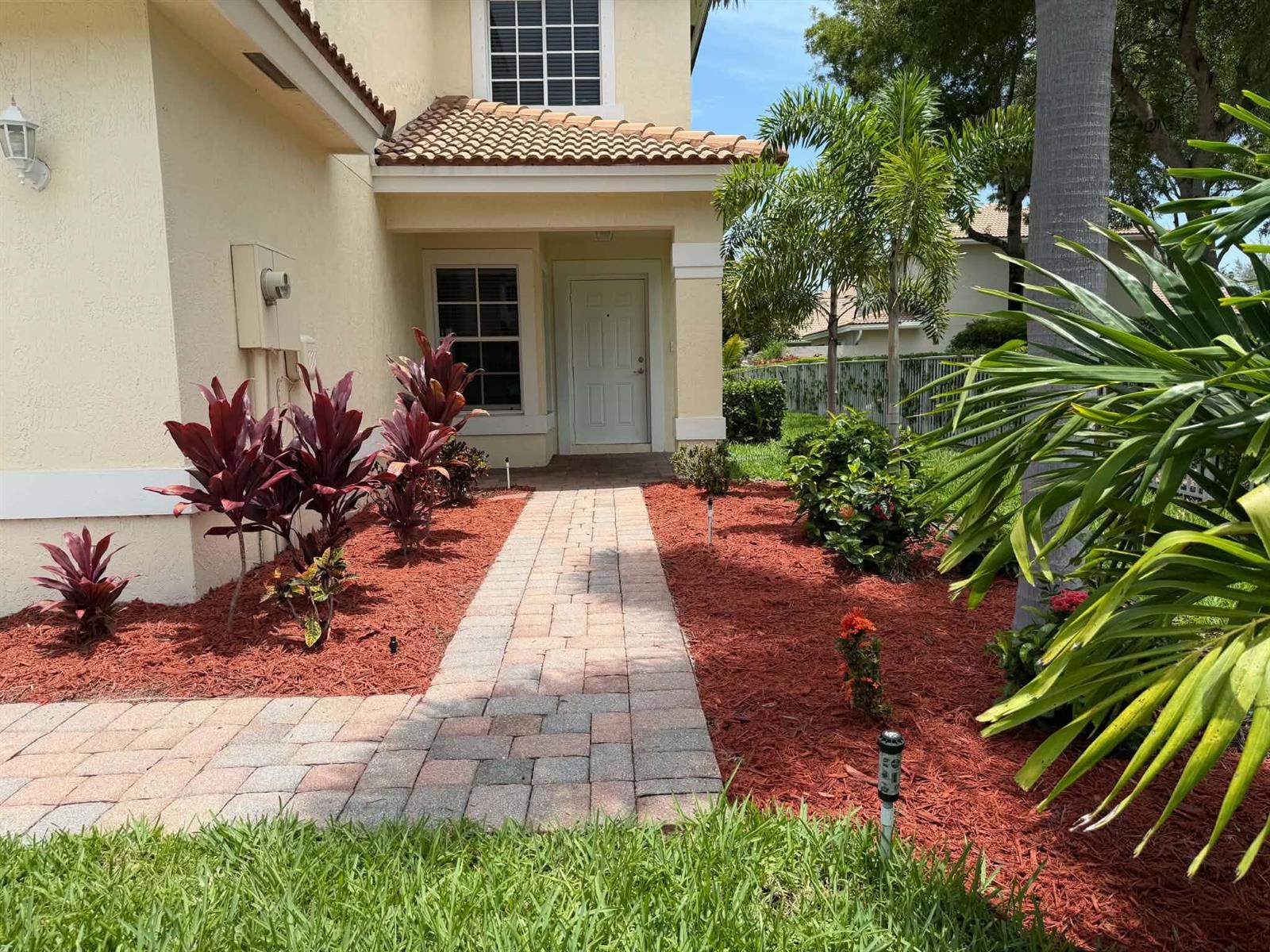 A paved walkway leads to the front entrance of a house with red mulch landscaping — 6355 Adriatic Way, West Palm Beach FL 33413, WEST PALM BEACH, FL