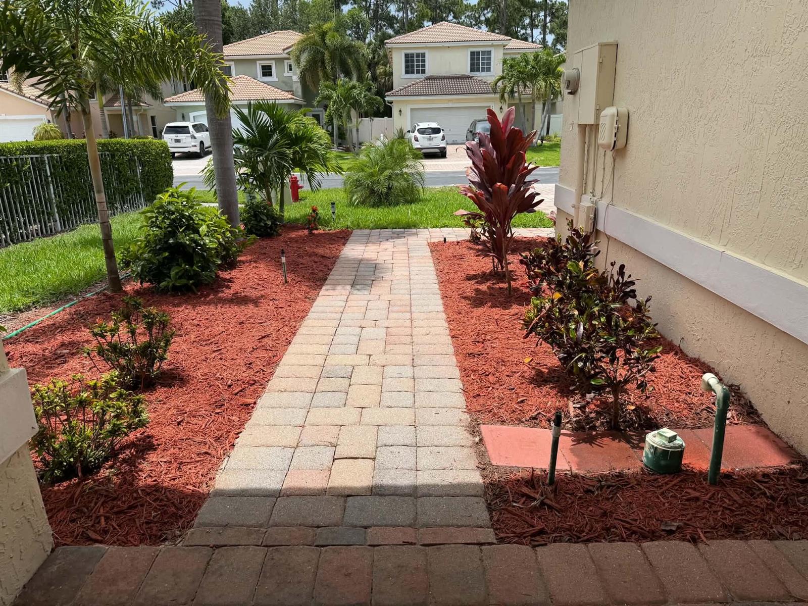 A paved walkway leads through a landscaped front yard with red mulch and various plants — 6355 Adriatic Way, West Palm Beach FL 33413, WEST PALM BEACH, FL
