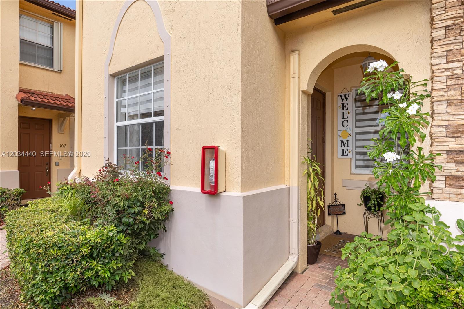 The exterior of a stucco townhouse features a front entrance, a window, and landscaping — 1490 NE 33rd Rd # 18, Homestead FL 33033, HOMESTEAD, FL
