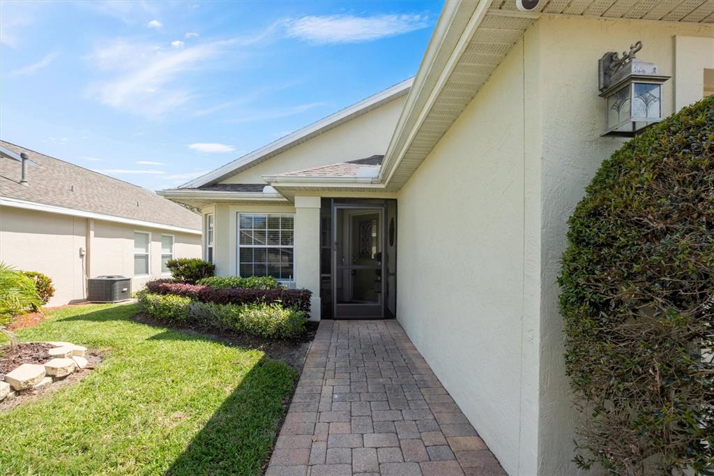 A paved walkway leads to the front entrance of a house with a screen door — 3905 OSPREY POINTE CIRCLE, WINTER HAVEN, FL