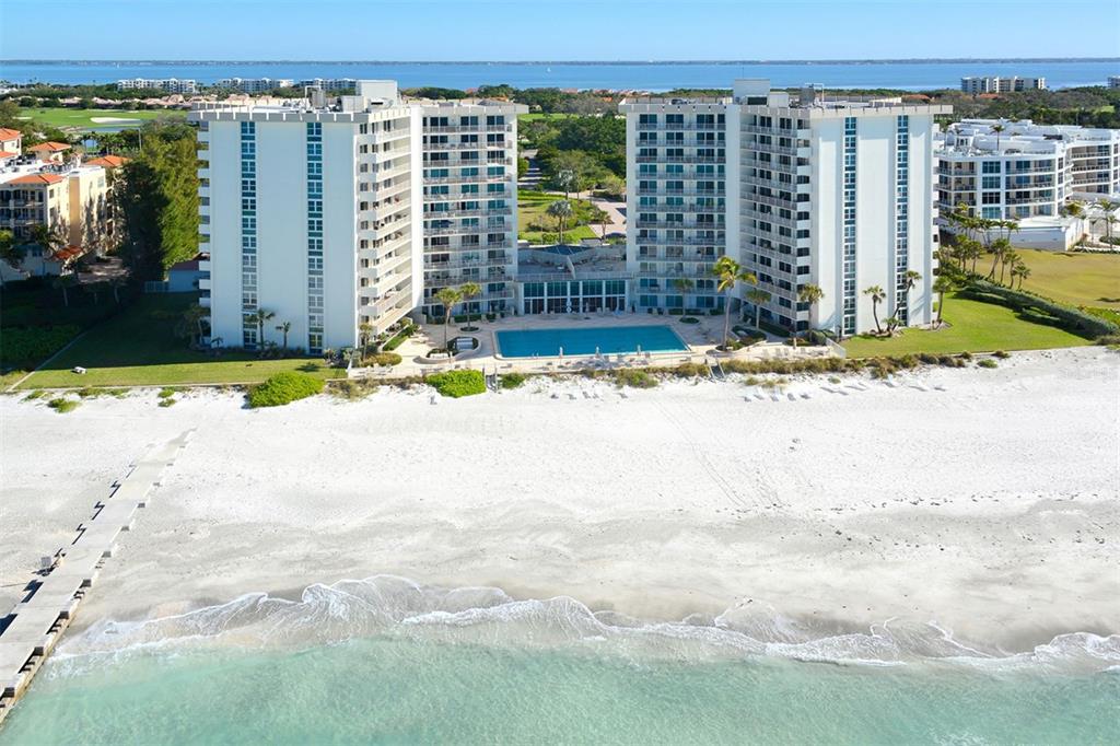 An aerial view shows a multi-story beachfront condominium building with a pool and sandy beach — 2301 GULF OF MEXICO DRIVE UNIT 12N, LONGBOAT KEY, FL