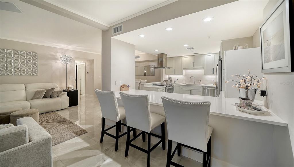 A modern kitchen with white cabinetry and a breakfast bar overlooks a living room area — 2301 GULF OF MEXICO DRIVE UNIT 12N, LONGBOAT KEY, FL