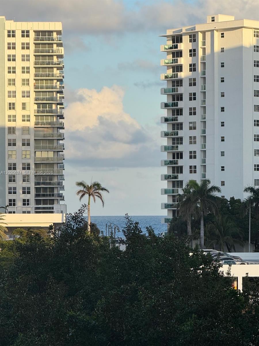 An exterior view shows two tall white apartment buildings framing a view of the ocean — 800 Parkview Dr # 406, Hallandale Beach FL 33009, HALLANDALE BEACH, FL