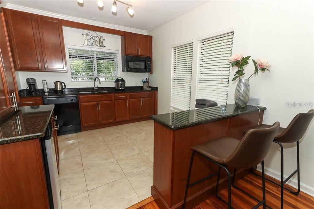 A kitchen features dark wood cabinets, granite countertops, tile flooring, and a breakfast bar — 1442 PALM AVENUE, WINTER PARK, FL