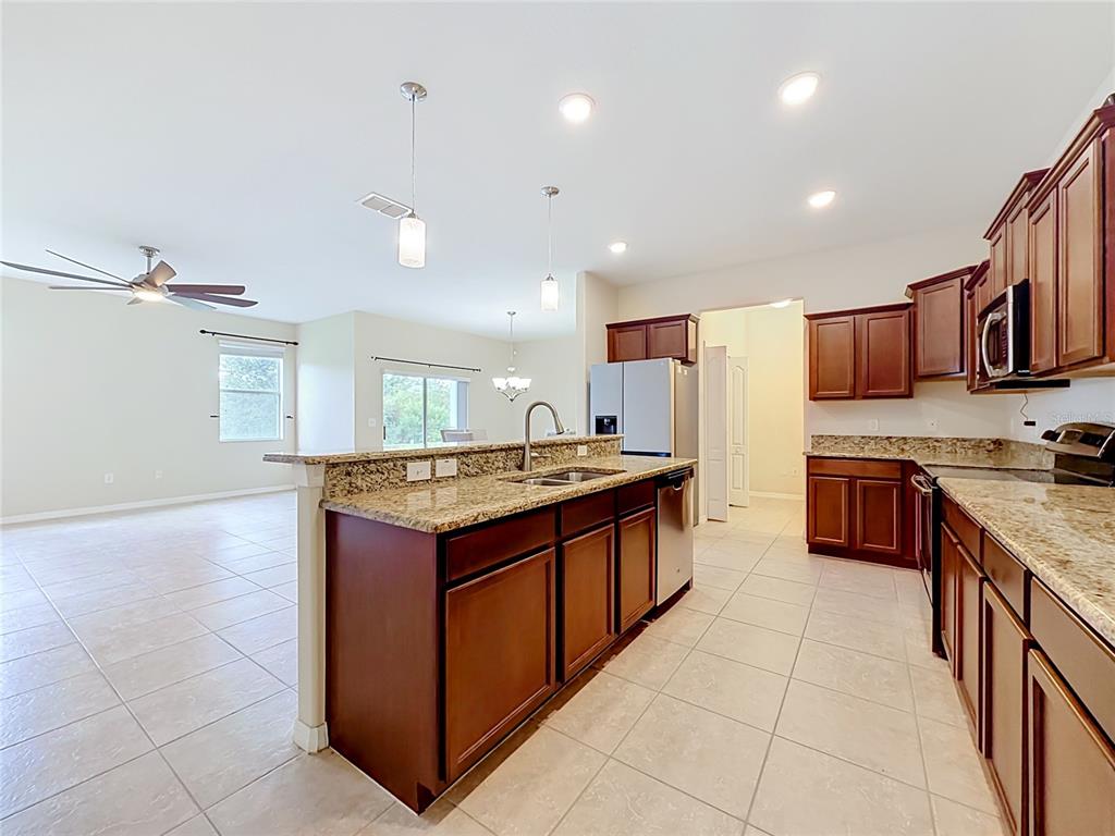 A kitchen with dark wood cabinets, granite countertops, and tile flooring opens to a living area — 3554 RODRICK CIRCLE, ORLANDO, FL