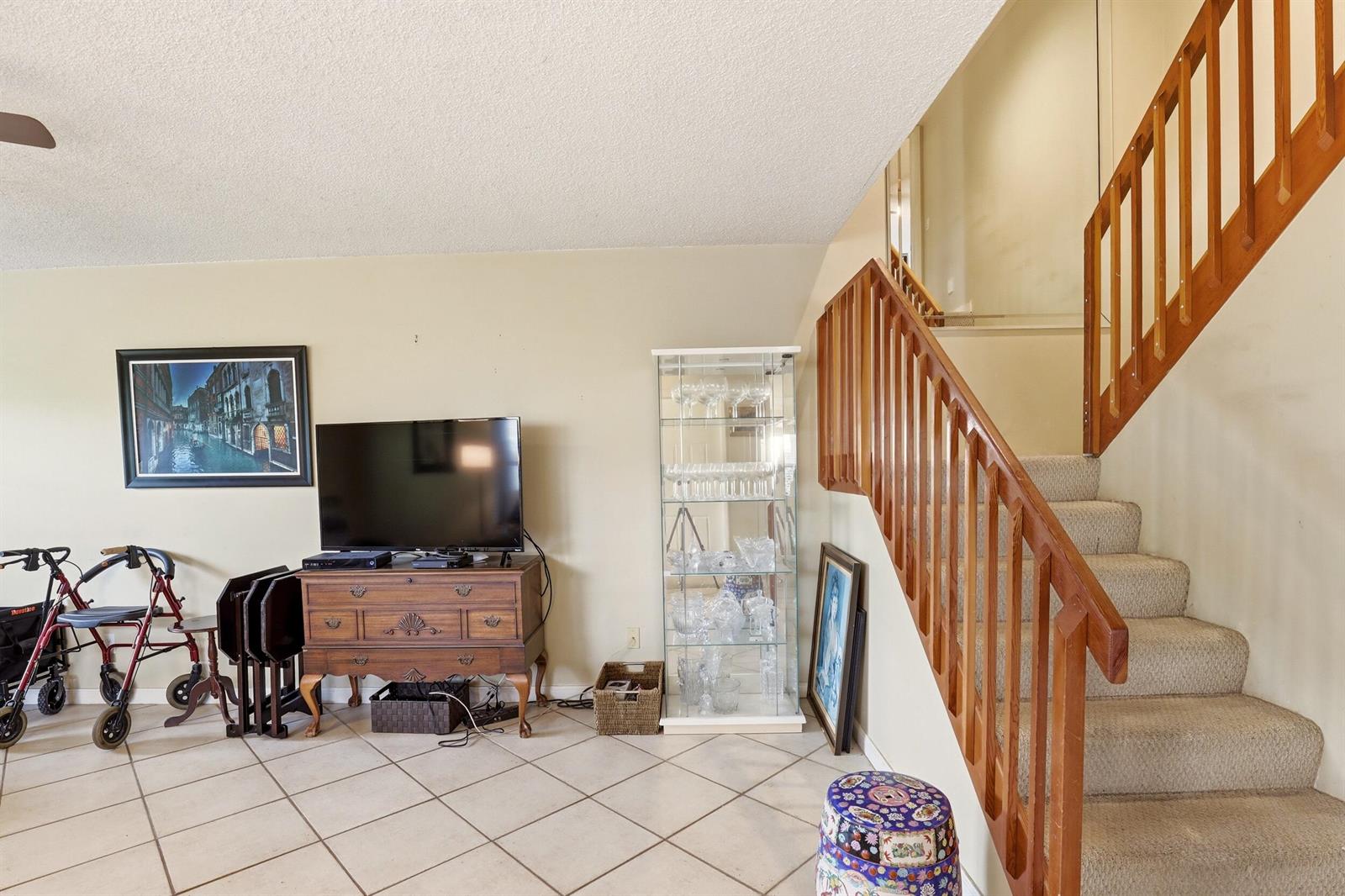 A living room features a wooden staircase, a television on a dresser, and tile flooring — 6604 Dryden Court # D, Boynton Beach FL 33436, BOYNTON BEACH, FL