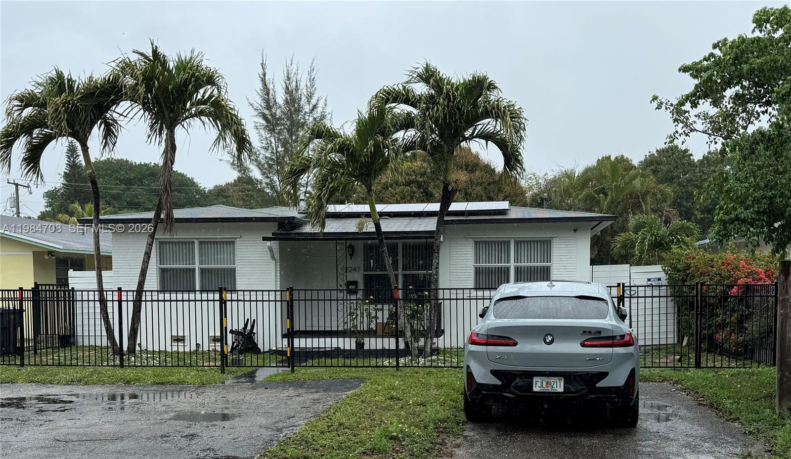 A backyard features a wooden deck, stone pathways, and large trees beside a white house — 2247 Jackson St, Hollywood FL 33020, HOLLYWOOD, FL