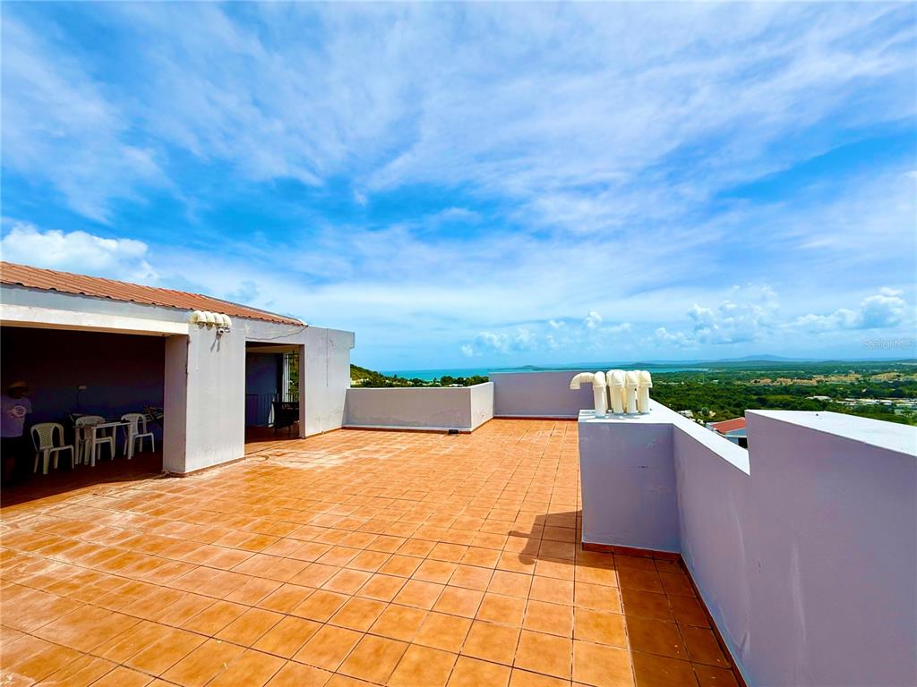 A tiled rooftop terrace overlooks a coastal landscape under a bright blue sky — PH-7 LA COSTA APTS UNIT H-7, FAJARDO, PR