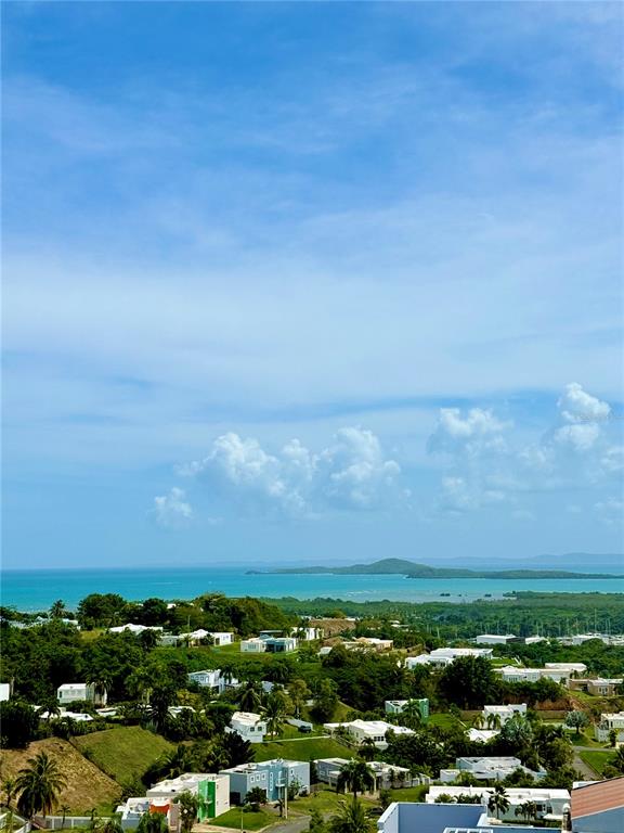 An elevated view shows a coastal landscape with scattered houses, lush greenery, and the ocean — PH-7 LA COSTA APTS UNIT H-7, FAJARDO, PR