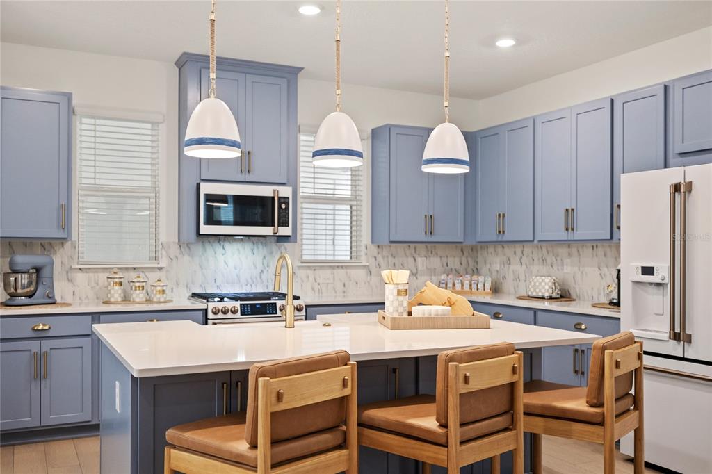 A kitchen features blue cabinets, white countertops, a marble backsplash, and three pendant lights — 16186 HONEY HARVEST STREET, WINTER GARDEN, FL