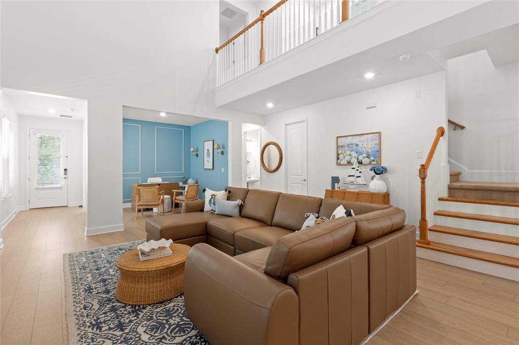 A living room features a brown sectional sofa, a blue accent wall, and a staircase — 16186 HONEY HARVEST STREET, WINTER GARDEN, FL