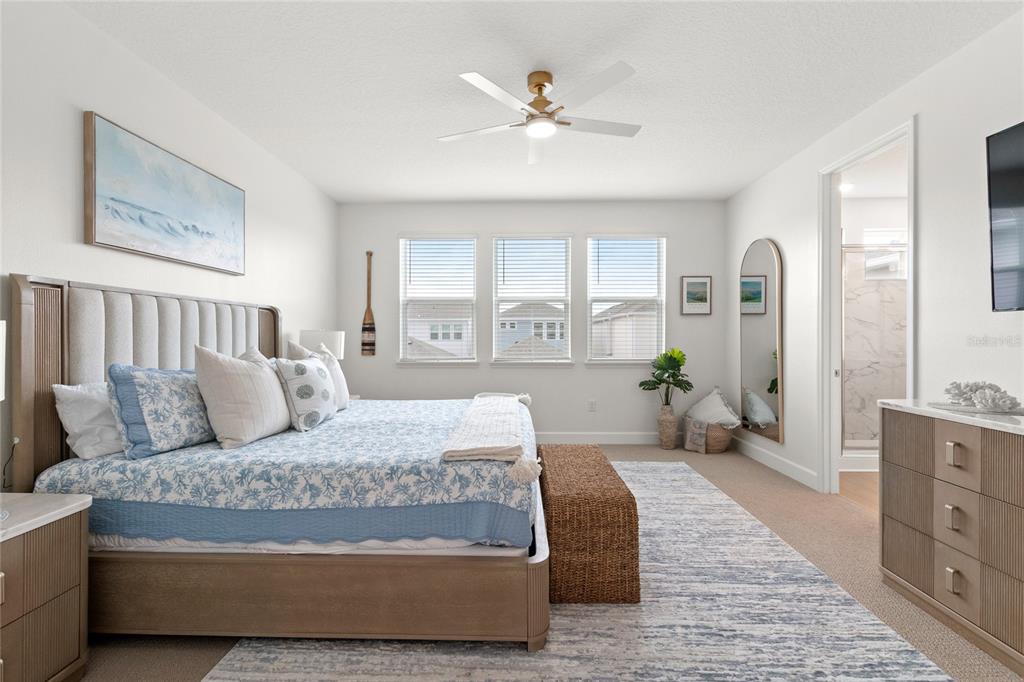 A bedroom features a king bed, a woven bench, a ceiling fan, and an attached bathroom — 16186 HONEY HARVEST STREET, WINTER GARDEN, FL