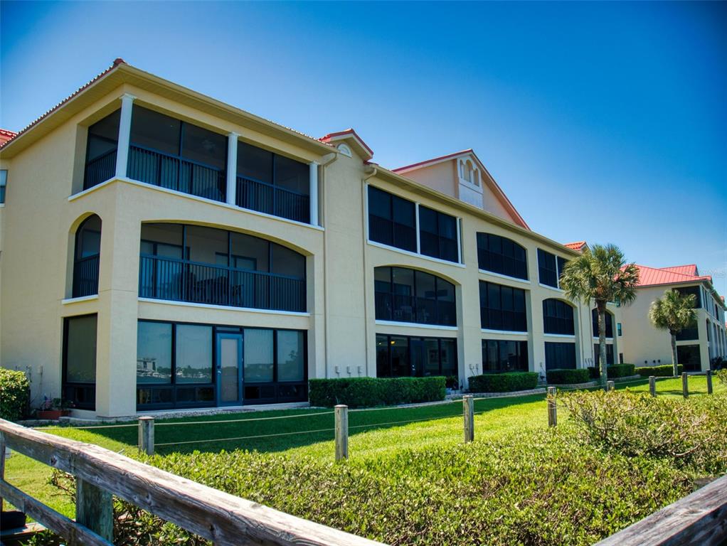 An exterior view of a multi-story apartment building with screened balconies and a grassy lawn — 444 BOUCHELLE DRIVE UNIT 201, NEW SMYRNA BEACH, FL