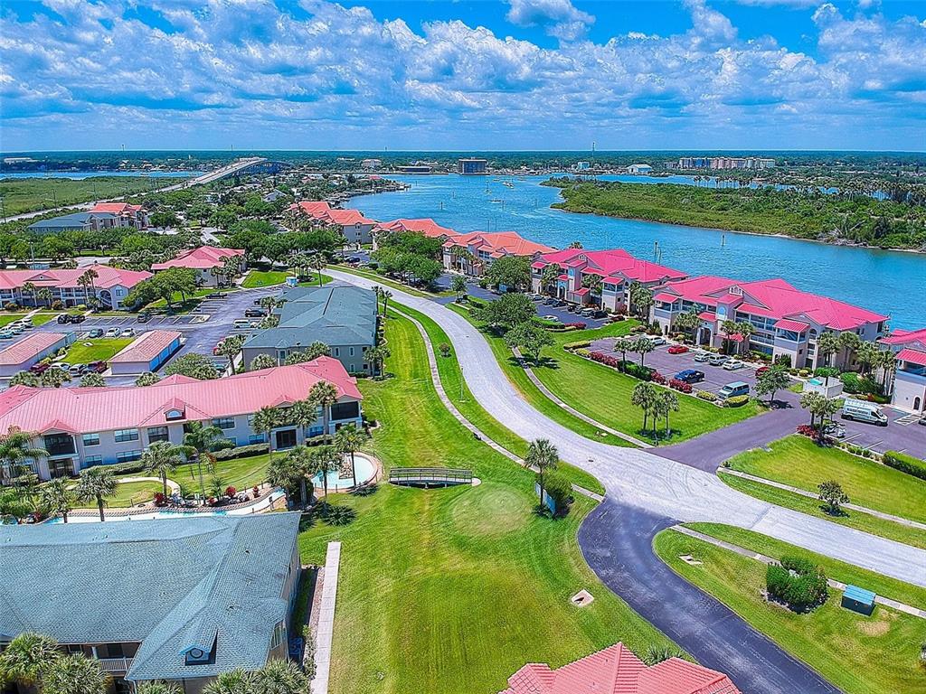 An aerial view shows a waterfront residential complex with red-roofed buildings and a winding road — 444 BOUCHELLE DRIVE UNIT 201, NEW SMYRNA BEACH, FL