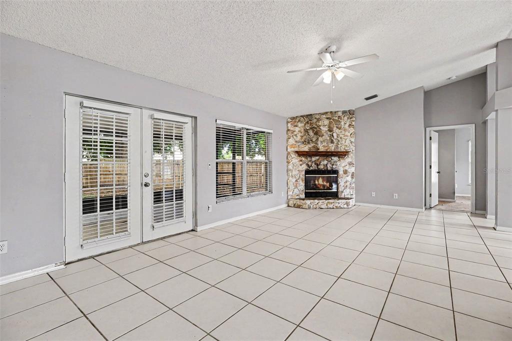 A living room with light tile flooring, a stone fireplace, and glass patio doors — 805 TOPAZ DRIVE, ROCKLEDGE, FL