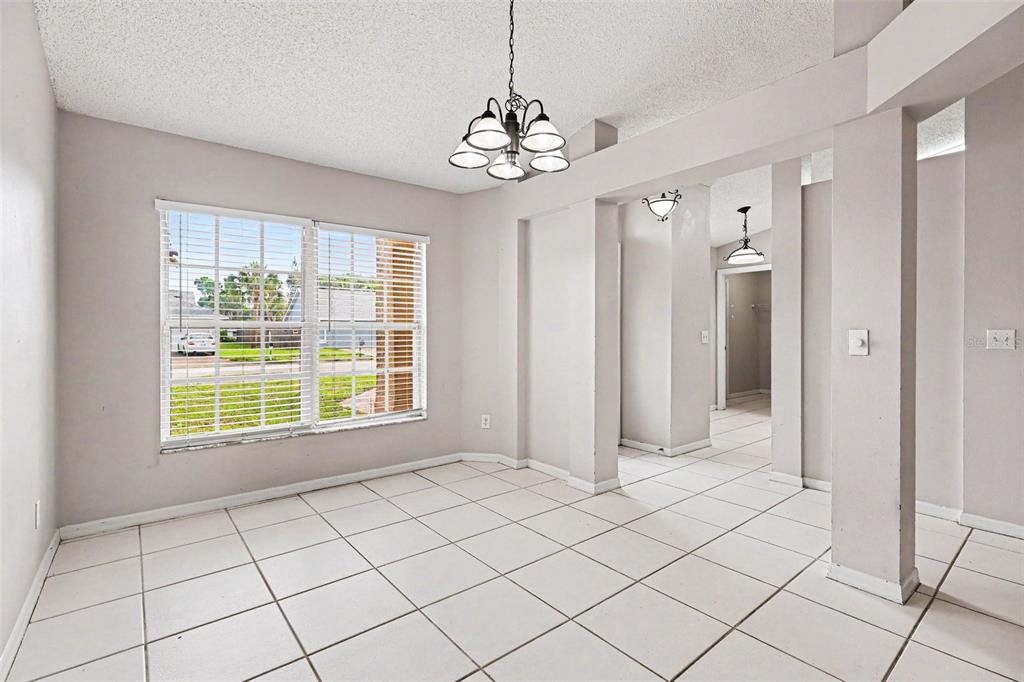 A dining room with white tile flooring, a chandelier, and a large window with blinds — 805 TOPAZ DRIVE, ROCKLEDGE, FL