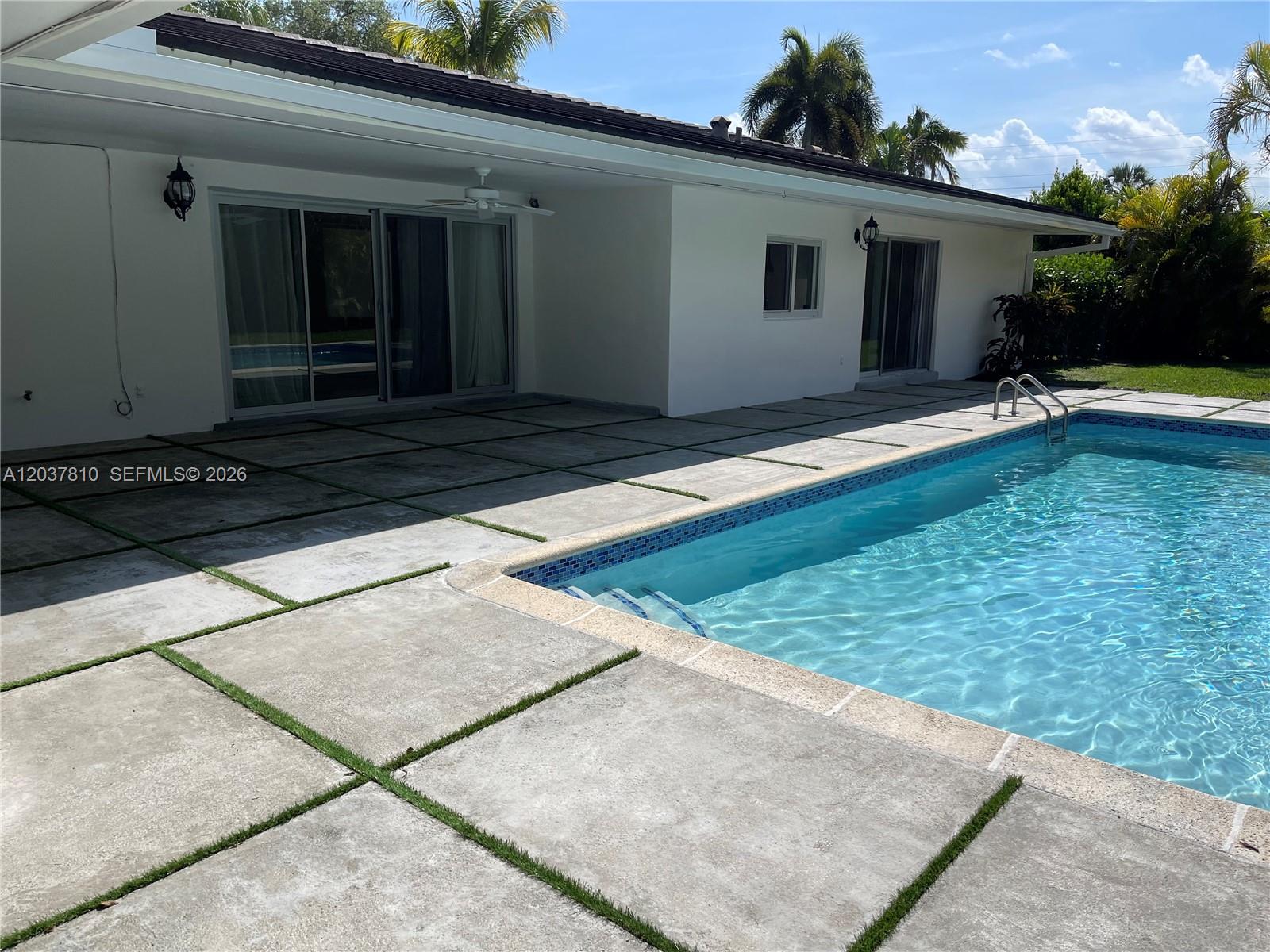 A swimming pool sits adjacent to a patio with concrete pavers and artificial grass joints — 7361 SW 117th Ter, Pinecrest FL 33156, PINECREST, FL