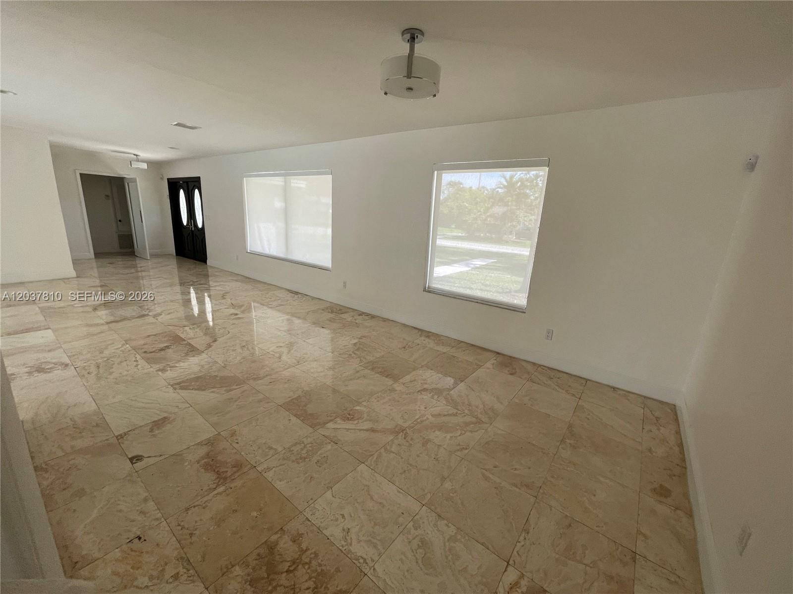 An empty room features large beige floor tiles, white walls, and two windows — 7361 SW 117th Ter, Pinecrest FL 33156, PINECREST, FL