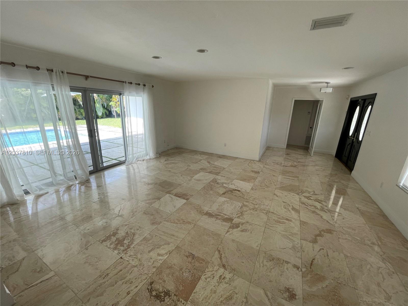 An empty room features polished stone tile flooring, white walls, and sliding glass doors — 7361 SW 117th Ter, Pinecrest FL 33156, PINECREST, FL