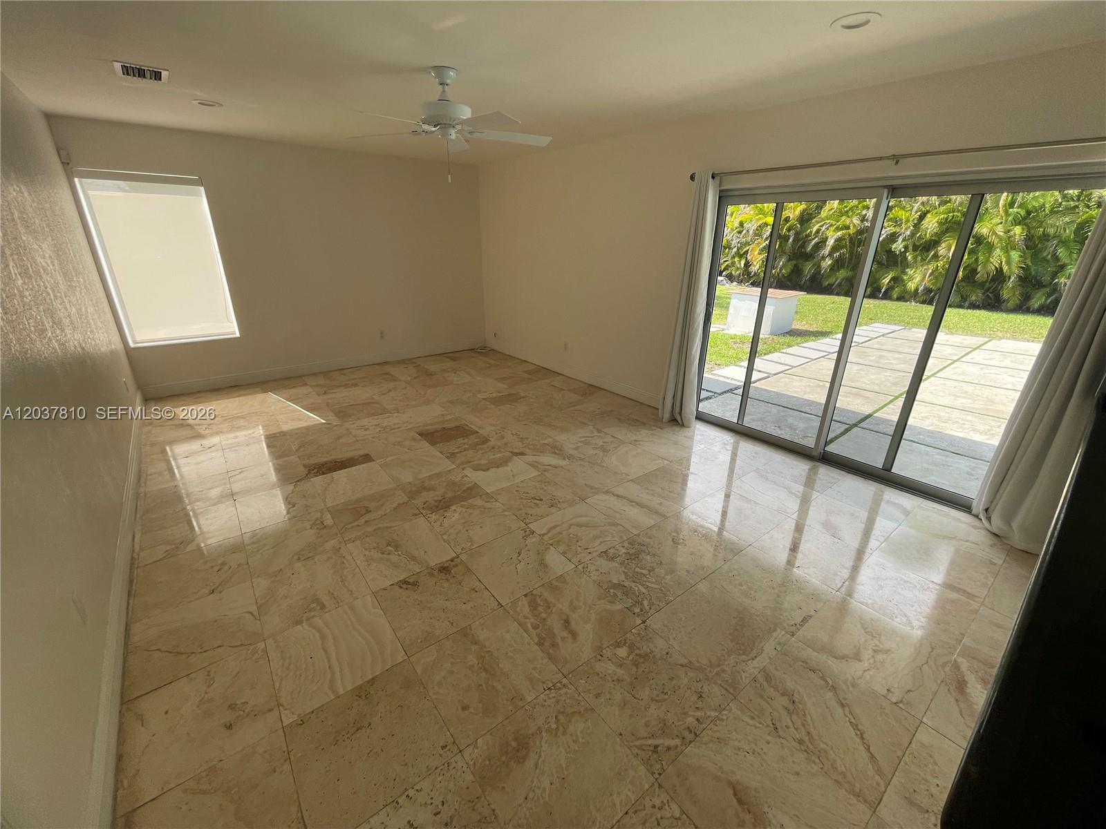 A spacious room features polished stone tile flooring, a ceiling fan, and sliding glass doors — 7361 SW 117th Ter, Pinecrest FL 33156, PINECREST, FL