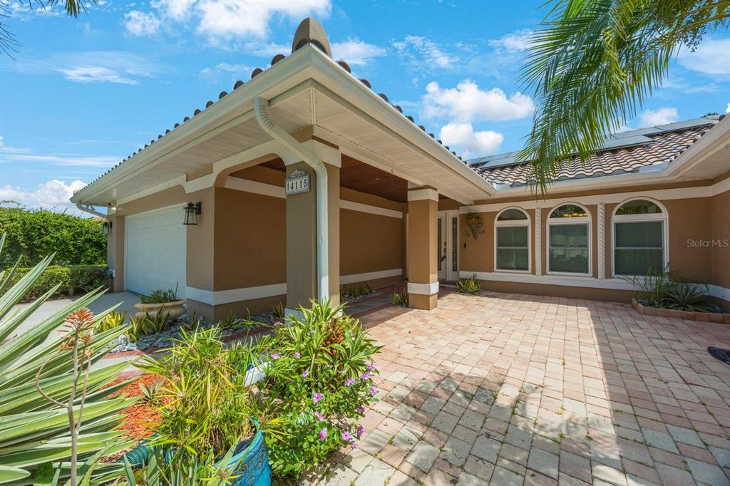 A tan house exterior features a paver driveway, a covered entryway, and three arched windows — 14115 HARBORWOOD DRIVE, LARGO, FL