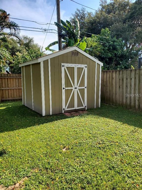 A tan wooden storage shed with white trim stands in a grassy backyard — 1637 WHITEWOOD DRIVE, CLEARWATER, FL