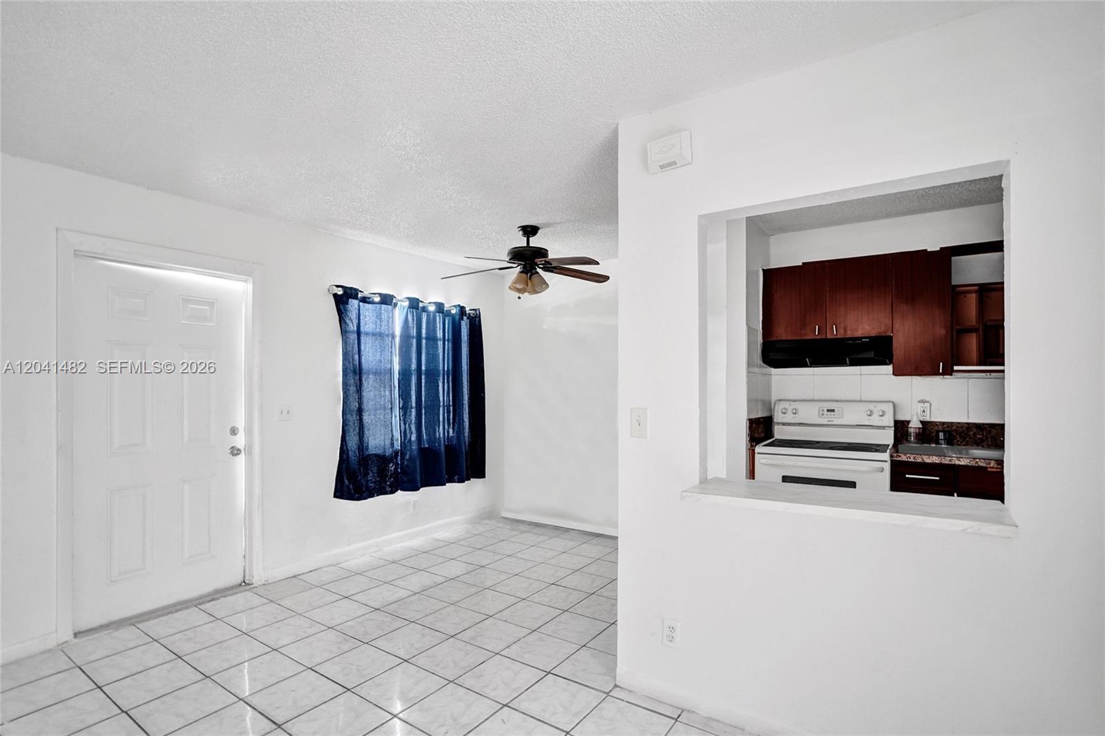 A room with white tile floors features a ceiling fan and a kitchen pass-through window — 841 SW 7th St # C, Pompano Beach FL 33060, POMPANO BEACH, FL