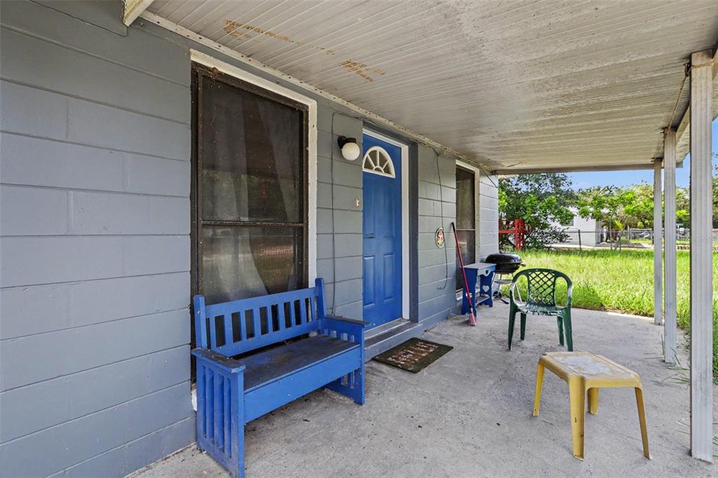 A covered concrete porch features a blue front door, a blue bench, and outdoor furniture — 4503 N 72ND STREET, TAMPA, FL