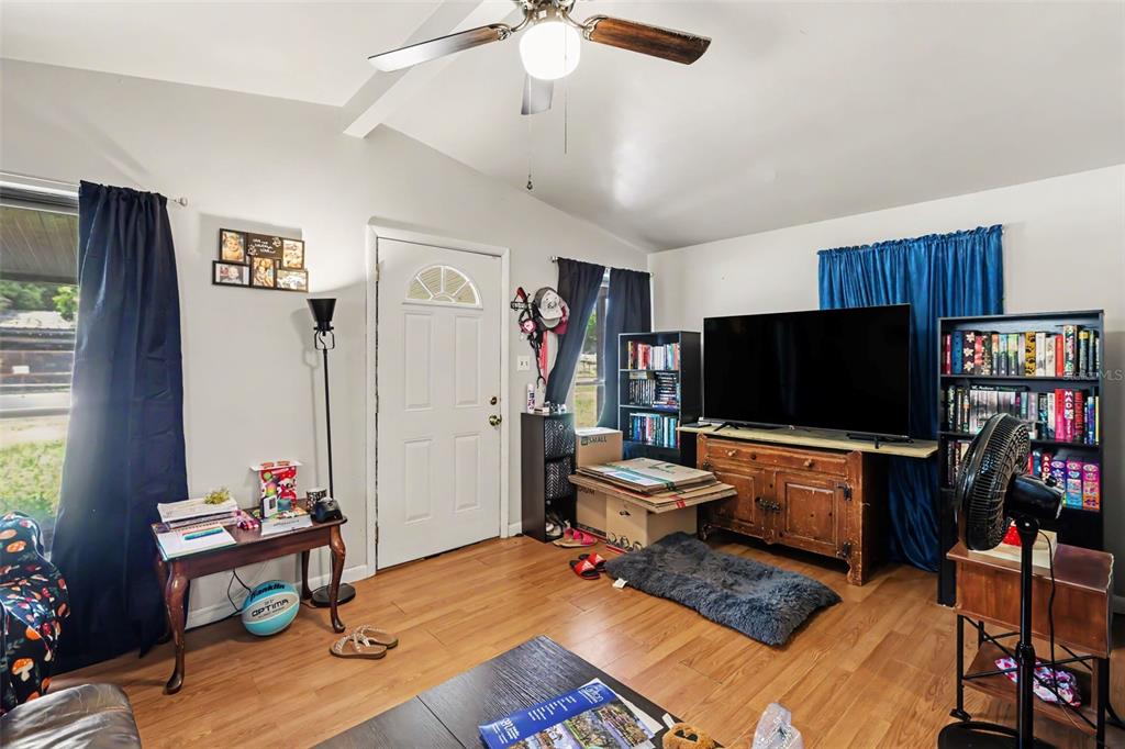 A living room features wood-look flooring, a ceiling fan, a television on a wooden console, and bookshelves — 4503 N 72ND STREET, TAMPA, FL