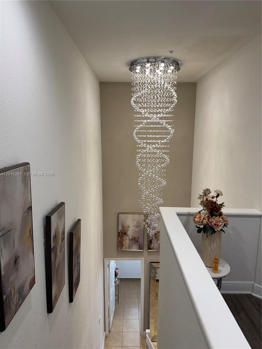 A tall, narrow stairwell features a multi-tiered crystal chandelier and framed wall art — 11942 SW 26th Ct, Miramar FL 33025, MIRAMAR, FL