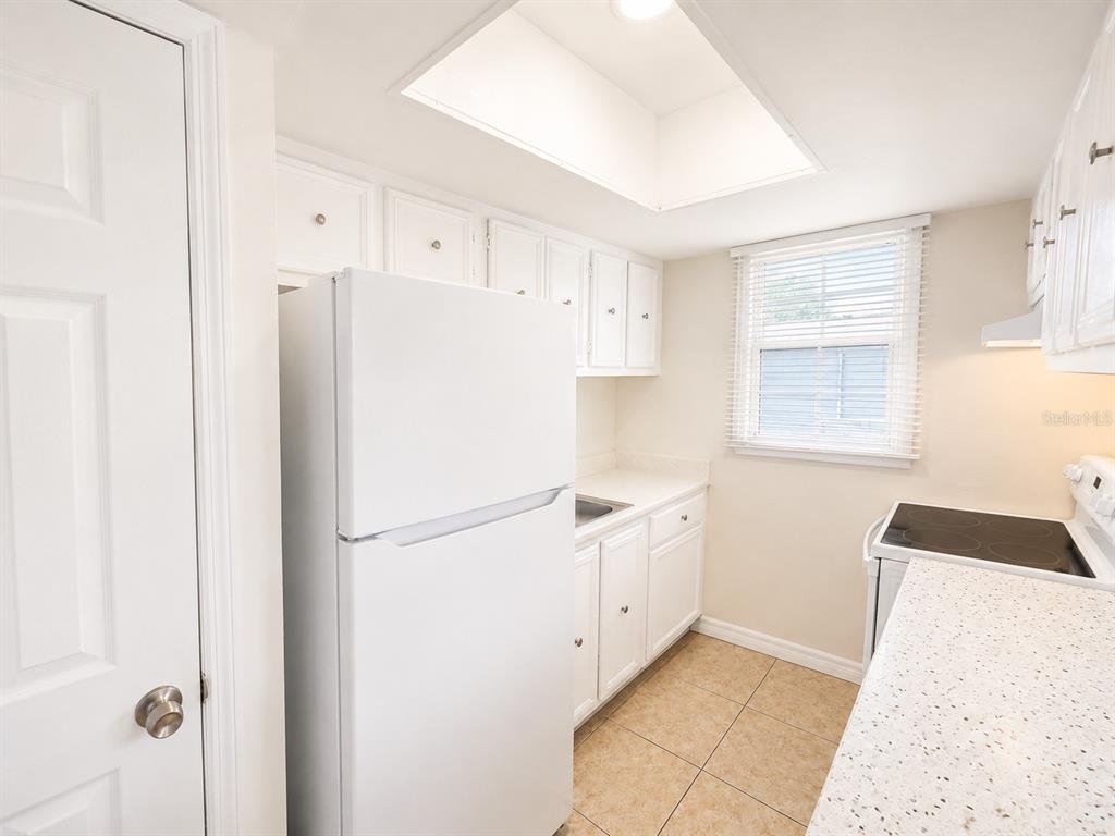 A white kitchen features a refrigerator, speckled countertops, white cabinets, and a skylight — 2759 L B MCLEOD ROAD UNIT C, ORLANDO, FL