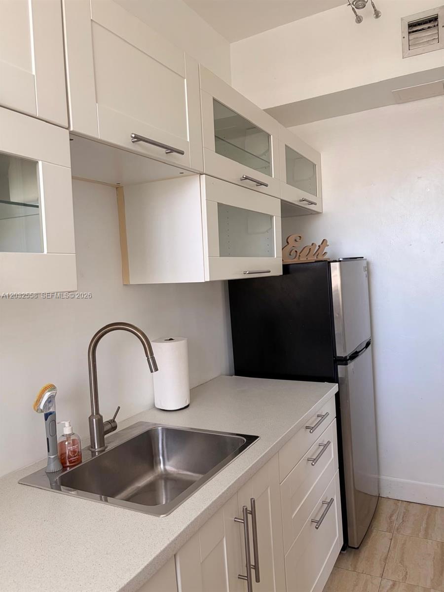 A small kitchen features white cabinets, a stainless steel sink, and a black refrigerator — 900 16th St # 301, Miami Beach FL 33139, MIAMI BEACH, FL