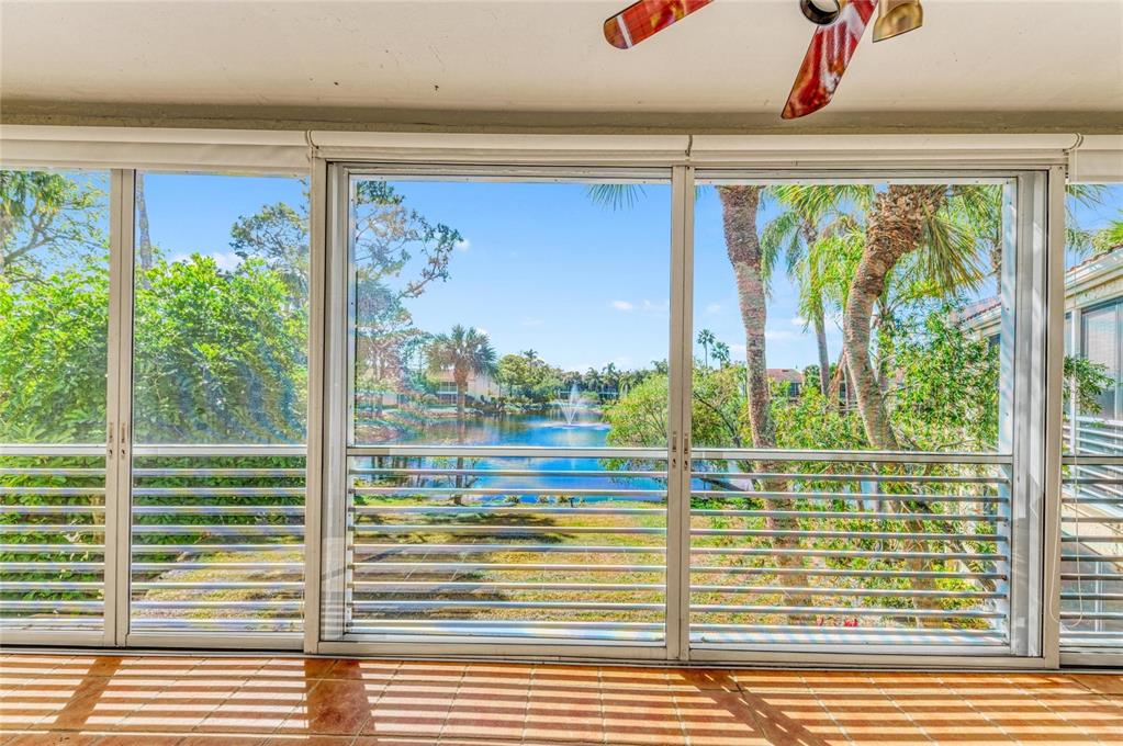 A sunroom with tiled floors and large sliding glass doors overlooking a pond and fountain — 6101 34TH STREET W UNIT 11G, BRADENTON, FL