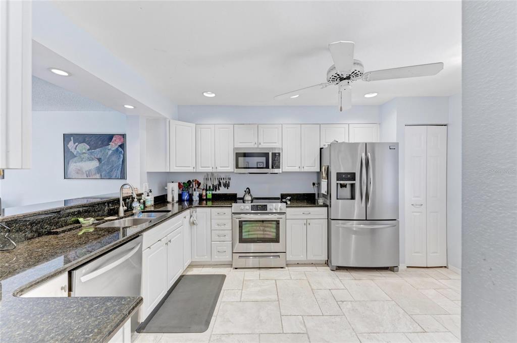 A kitchen features white cabinets, stainless steel appliances, dark granite countertops, and light tile flooring — 6101 34TH STREET W UNIT 11G, BRADENTON, FL
