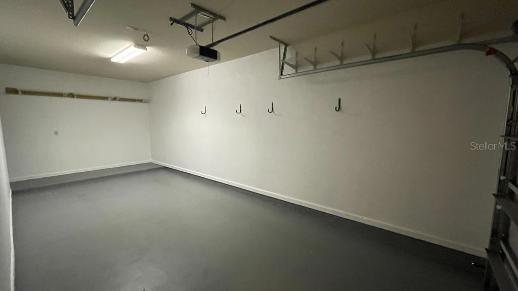 An empty garage features gray painted floors, white walls, and several wall-mounted storage hooks — 10539 VILLA VIEW CIRCLE UNIT 10539, TAMPA, FL