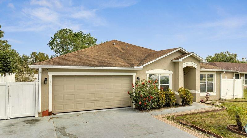 A tan, single-story house features a two-car garage, a front entrance, and white vinyl fencing — 639 MESILLA DRIVE, KISSIMMEE, FL