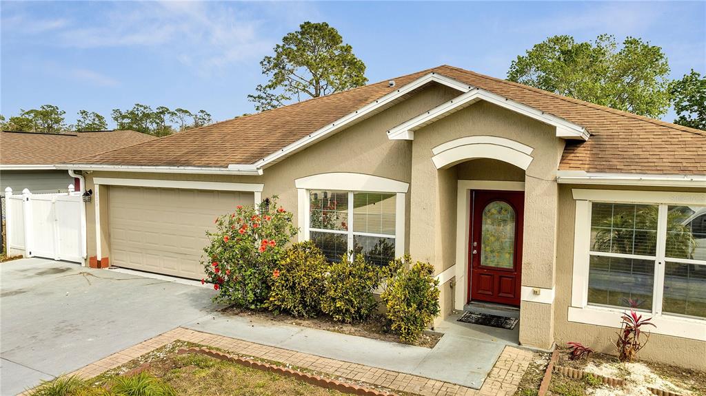 The exterior of a single-story house features a tan stucco facade, a red door, and a garage — 639 MESILLA DRIVE, KISSIMMEE, FL
