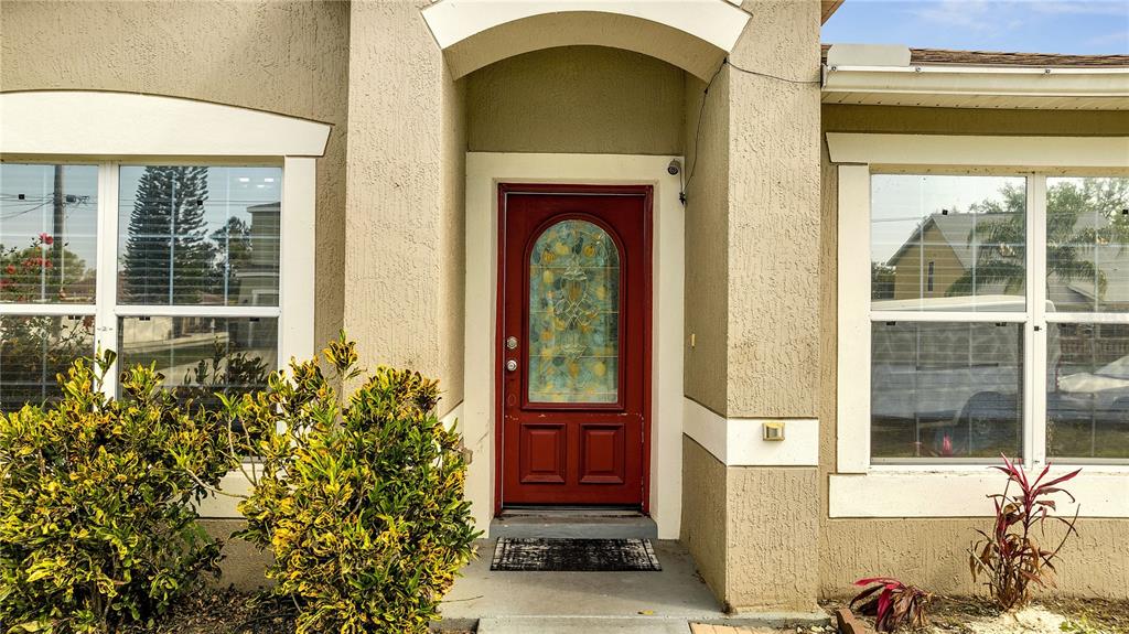 A red front door with a decorative glass insert is centered between two large windows — 639 MESILLA DRIVE, KISSIMMEE, FL