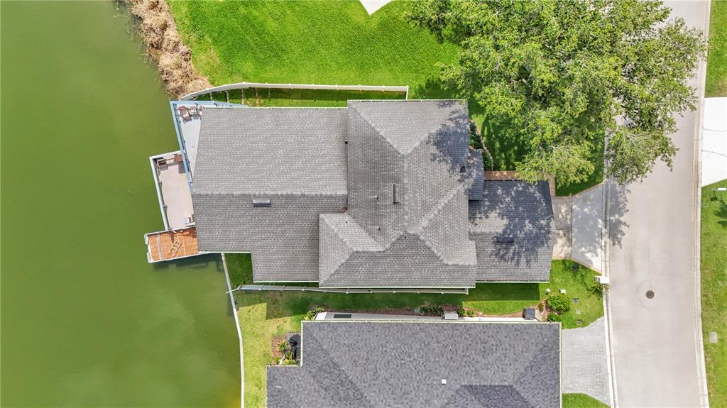 An aerial view shows a house with a gray shingled roof situated beside a lake — 601 PENINSULAR DRIVE, LAKELAND, FL