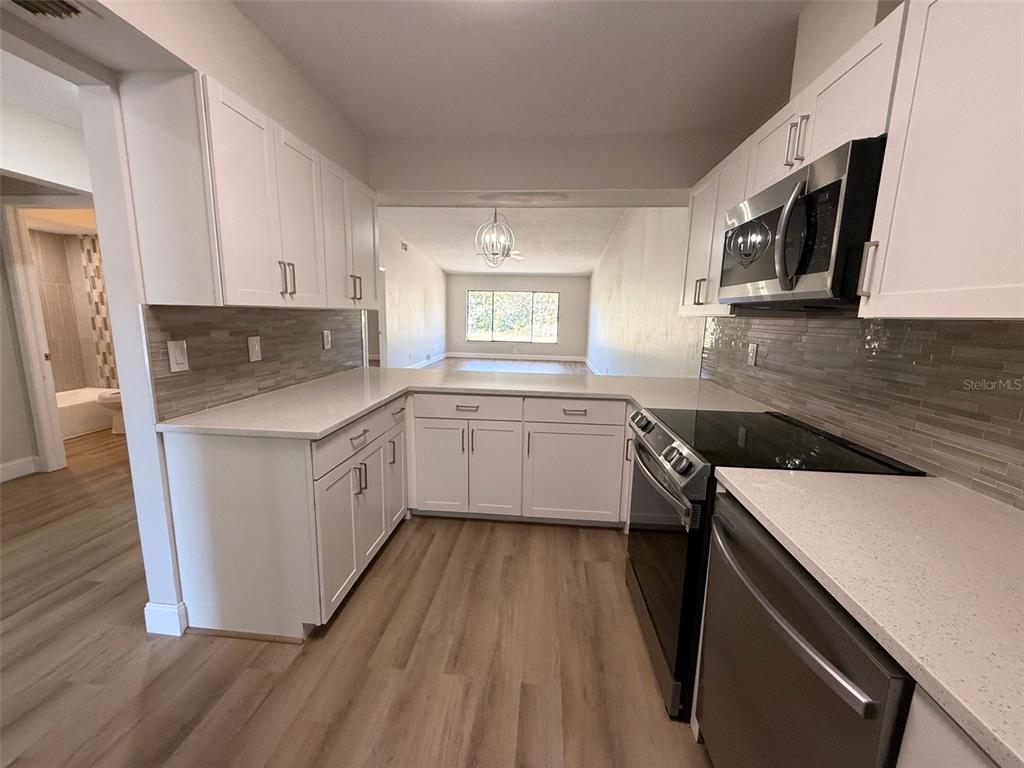 A kitchen with white cabinets, light countertops, and stainless steel appliances overlooks a living area — 3505 TARPON WOODS BOULEVARD UNIT J408, PALM HARBOR, FL