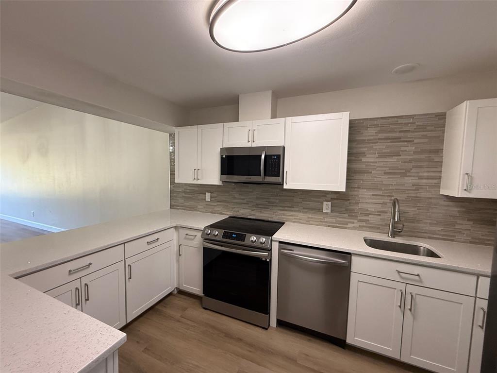 A kitchen featuring white cabinets, stainless steel appliances, a tiled backsplash, and light-colored countertops — 3505 TARPON WOODS BOULEVARD UNIT J408, PALM HARBOR, FL