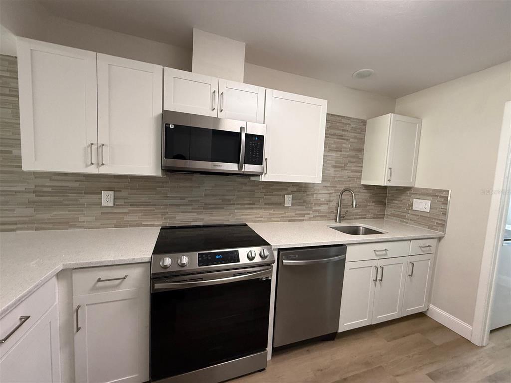 A kitchen features white cabinets, stainless steel appliances, a tiled backsplash, and light countertops — 3505 TARPON WOODS BOULEVARD UNIT J408, PALM HARBOR, FL