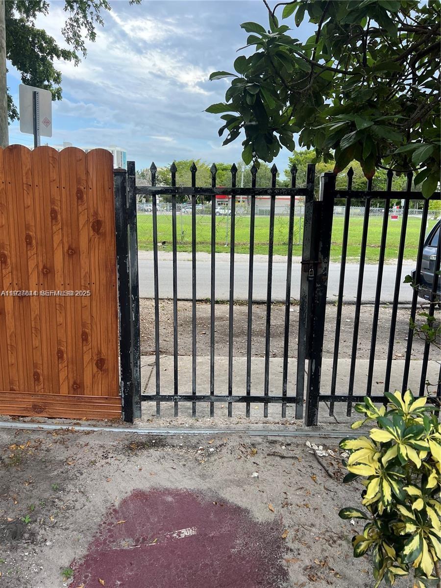 A black metal gate stands next to a wooden fence overlooking a grassy lot — 1581 NE 117 ST, Miami FL 33161, MIAMI, FL