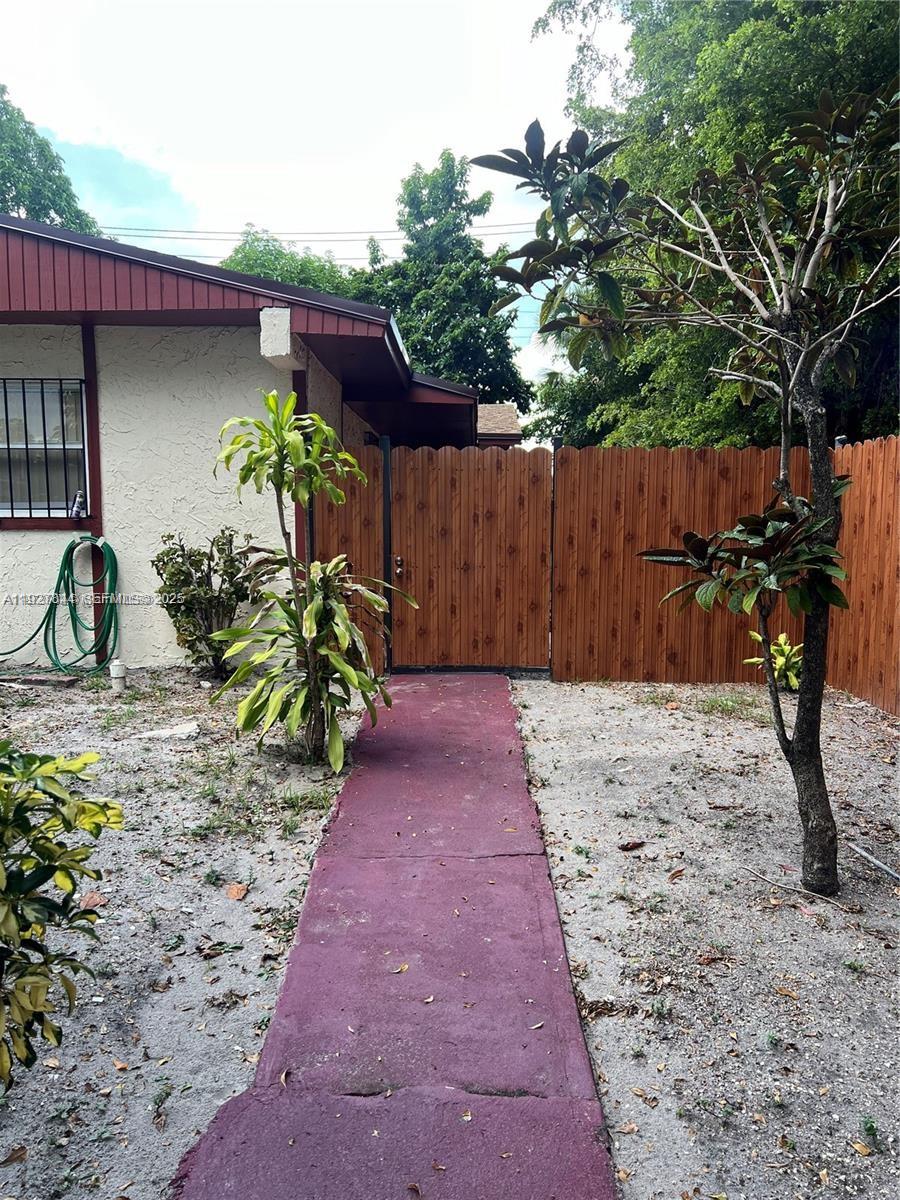 A red walkway leads to a wooden gate beside a house with a white exterior — 1581 NE 117 ST, Miami FL 33161, MIAMI, FL