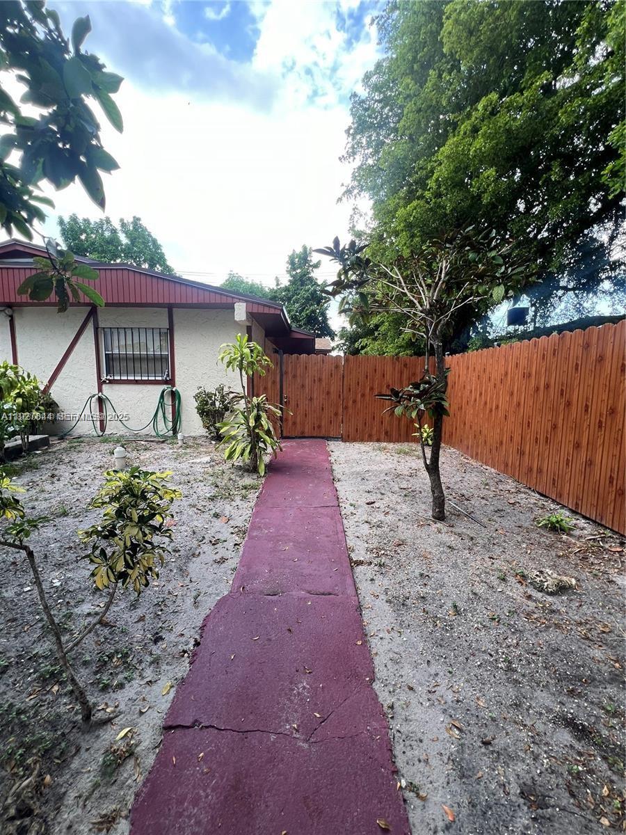 A red-painted walkway leads through a sandy yard toward a wooden fence and house — 1581 NE 117 ST, Miami FL 33161, MIAMI, FL