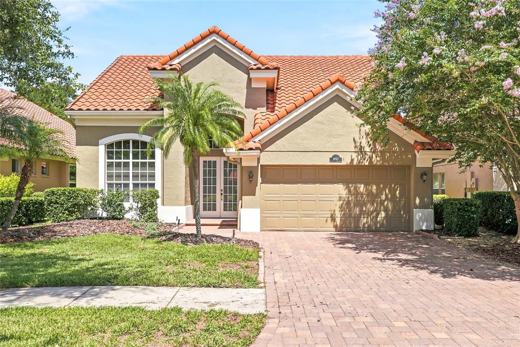 A single-story house with a tan stucco exterior, red tile roof, and brick paver driveway — 18912 PLACE MARQUETTE, LUTZ, FL
